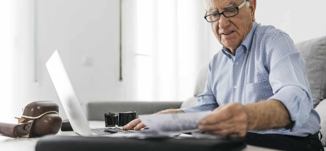 Senior man working with a computer and his old photo cameras and old photos